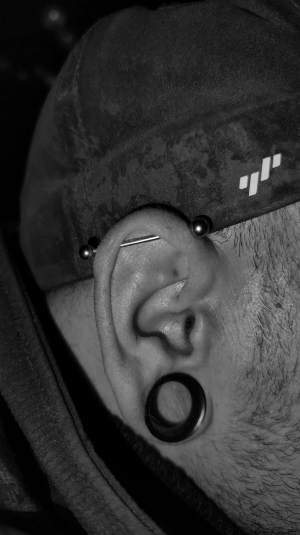 Seitenansicht eines Ohrs mit einem schwarzen Tunnel im gedehnten Ohrloch und einem Industrial-Piercing mit schwarzem Schmuck. Die Person trägt eine Mütze.